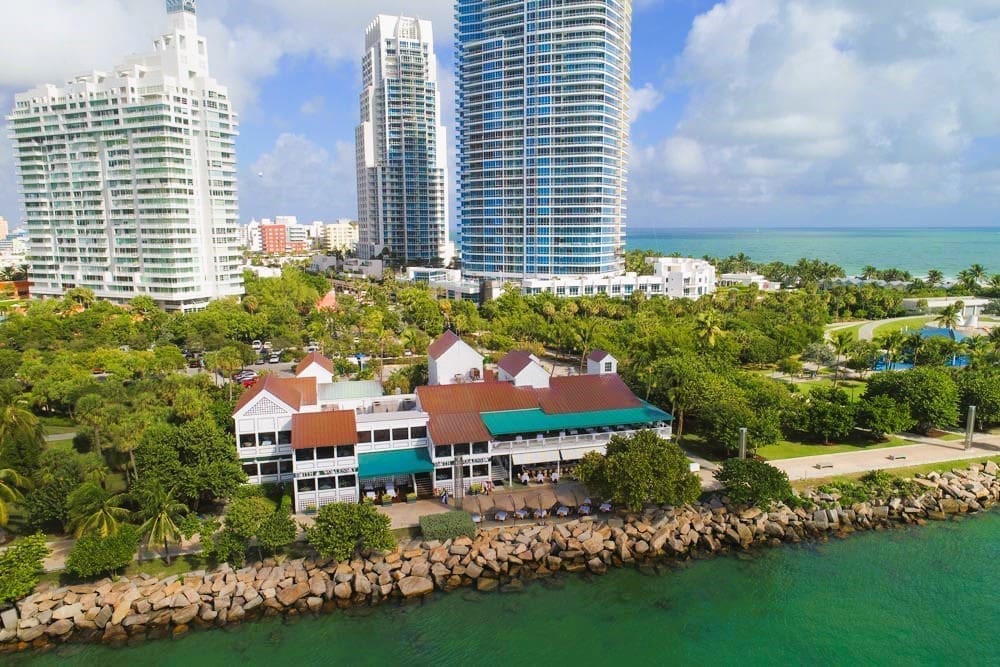 An aerial view of Smith & Wollensky restaurant and its outdoor seating at South Pointe Park, Miami Beach, with high-rise buildings, green spaces, and the ocean in the background.