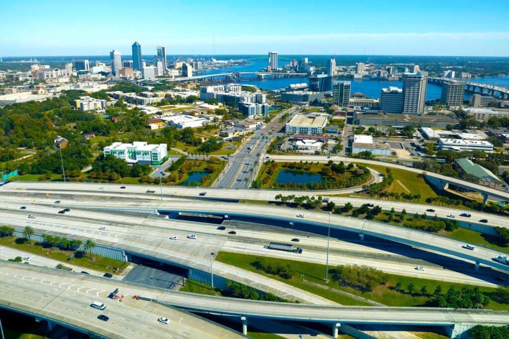 An aerial view of downtown Jacksonville, with Interstate 95 and its overpasses in the foreground, and the city skyline in the distance.