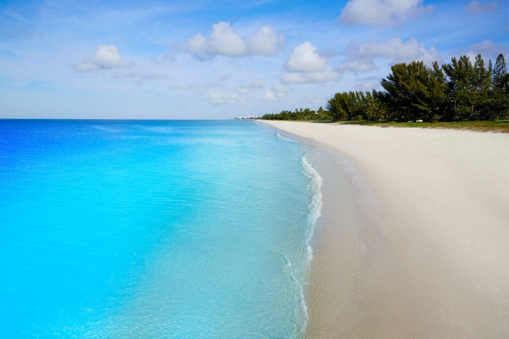 The pristine white sand and brilliant turquoise water of Naples Beach on a sunny day with a blue sky and clouds.
