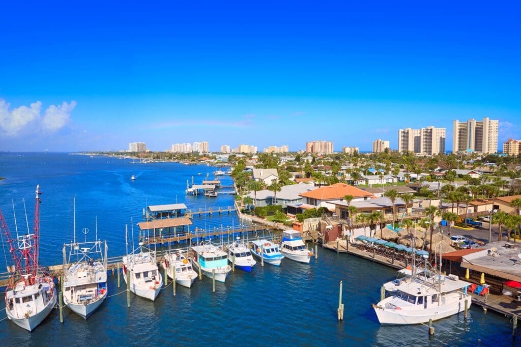 An aerial view of the Daytona Beach shoreline and skyline from Port Orange, with boats docked at a marina and buildings lining the coast.