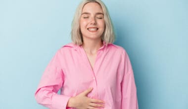 A young Caucasian woman gently touches her tummy while smiling softly, despite experiencing a slight discomfort in her upper abdomen