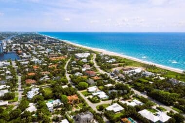 Aerial drone footage highlighting a beachside residential area in South Florida, featuring stunning turquoise waters set against a bright blue sky