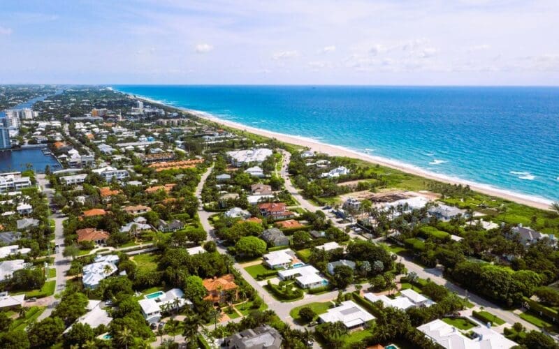 Aerial drone footage highlighting a beachside residential area in South Florida, featuring stunning turquoise waters set against a bright blue sky