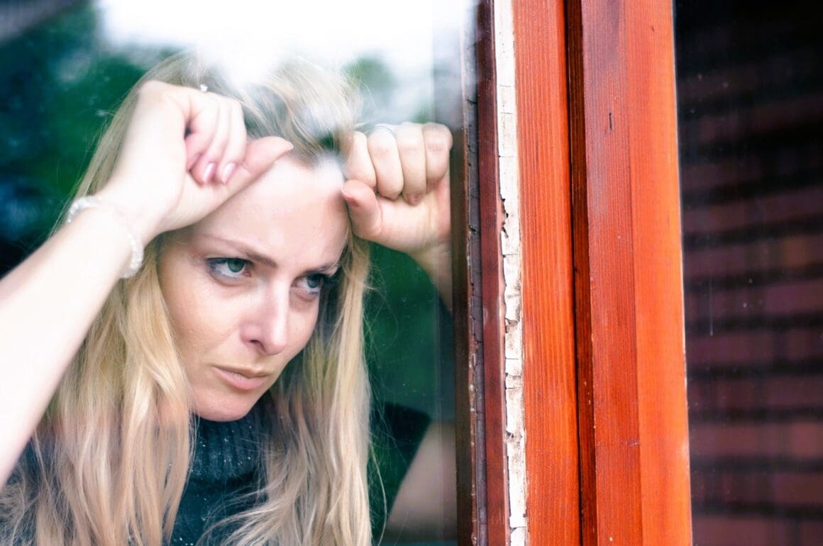 A frustrated woman stands by her window, irritated by the noise from her neighbor