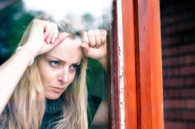 A frustrated woman stands by her window, irritated by the noise from her neighbor