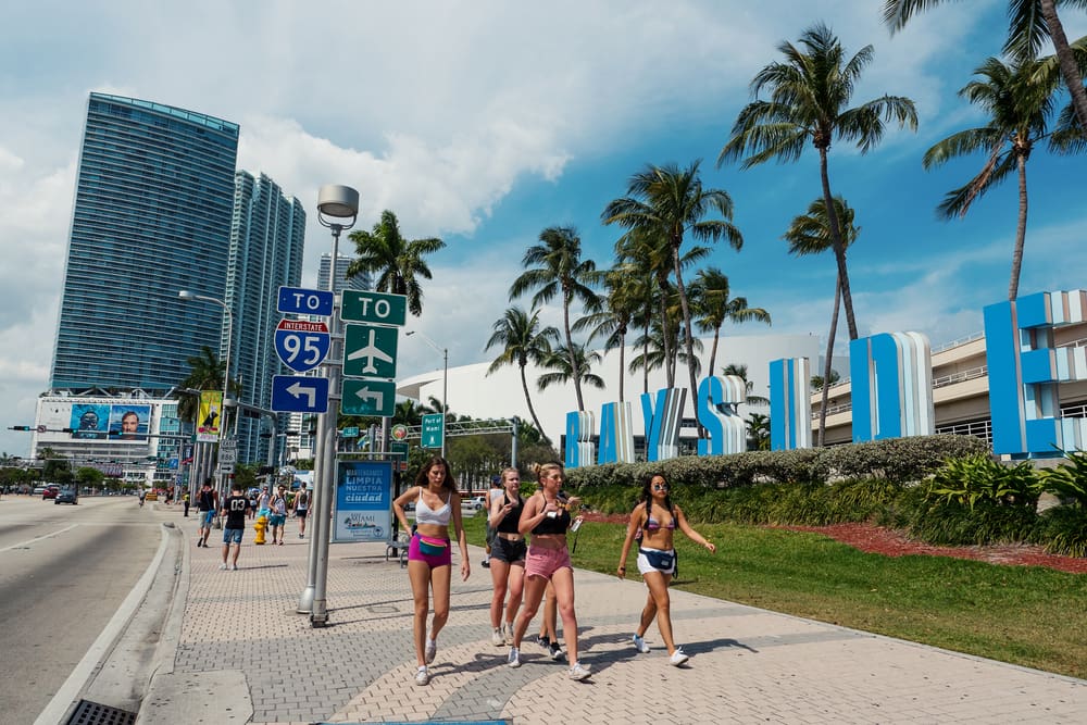 MIAMI - MARCH 18, 2016. Young women walking on the street going to Ultra Music Festival in front of Bayside Marketplace sign. By Shutterstock.com - pio3