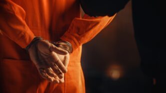 Arrested Handcuffed Convict at a Law and Justice Court Trial. Handcuffs on Accused Criminal in Orange Jail Jumpsuit. Law Offender Sentenced to Serve Jail Time.
