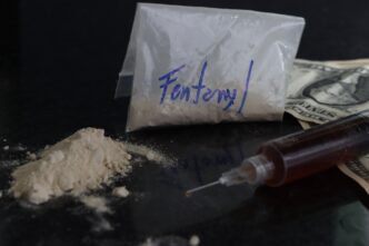 Dollar bills and a fentanyl powder pack with a syringe in a dark place showing the addiction of drugs