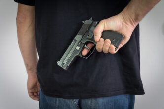 The man holding the gun in his hand behind his back. Illegal possession of weapons. By Shutterstock.com - Zoka74