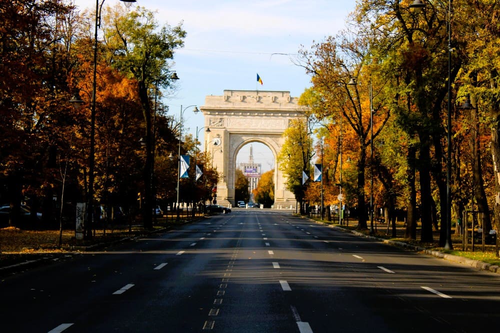 The Arcul de Triumf (Arch of Triumph) at the end of a tree-lined avenue with autumn colors in Bucharest, Romania.