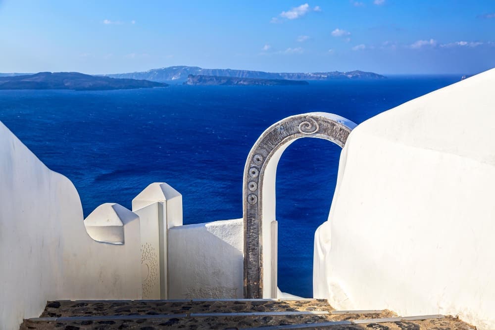A beautiful white-washed archway with intricate carvings frames a breathtaking view of the deep blue Aegean Sea and distant volcanic islands in Oia, Santorini, Greece.