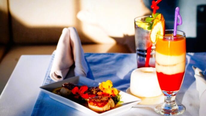 A beautifully presented meal with two drinks on a table, including a layered red, white, and orange cocktail and a plate with seared scallops garnished with edible flowers.