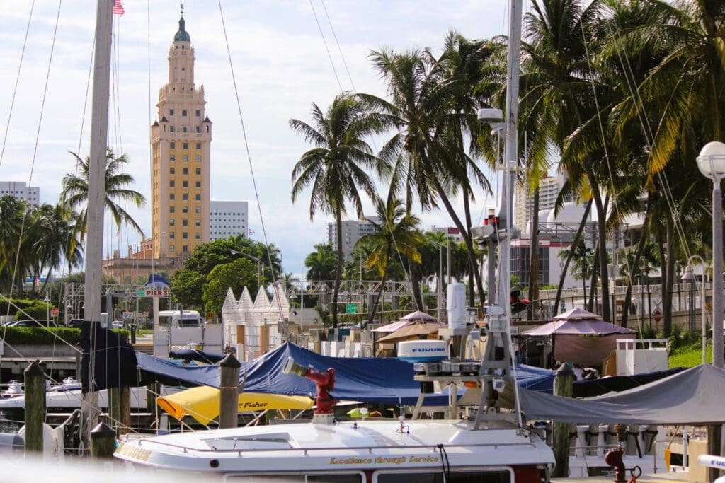 The iconic Freedom Tower in Miami stands tall behind a marina full of sailboats and palm trees