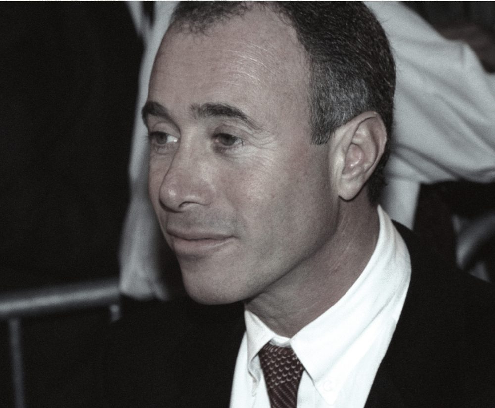 A man with short hair and a suit looks to the side while leaving a restaurant