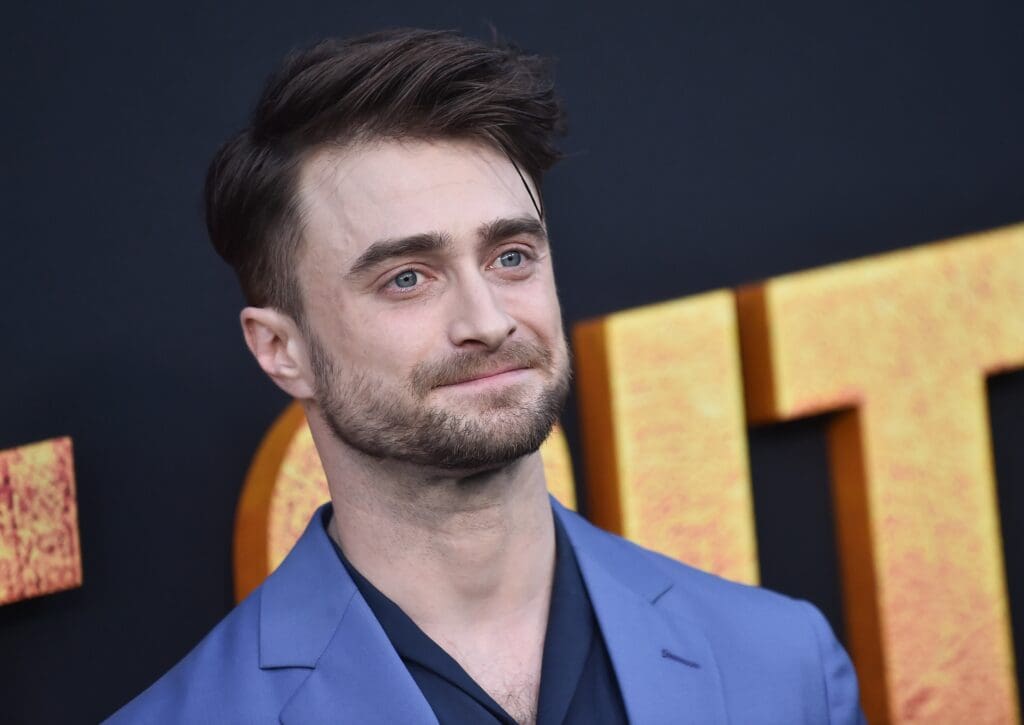 Close-up of actor Daniel Radcliffe with blue eyes and a beard, wearing a blue suit jacket at a film premiere event