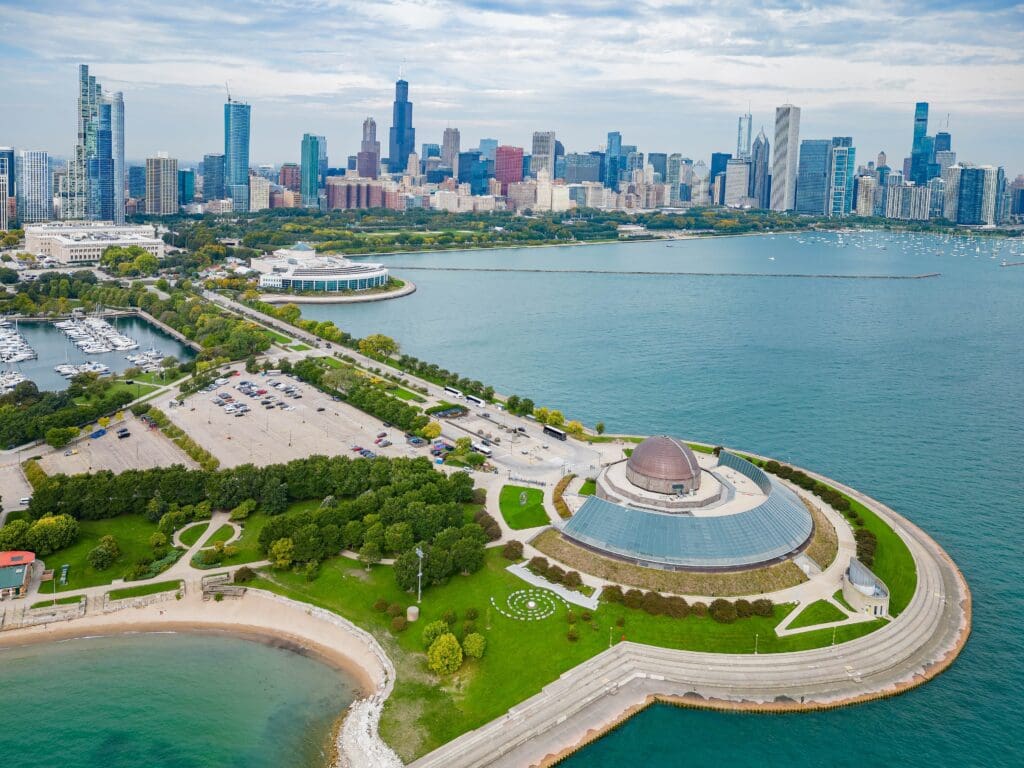 Aerial view of Chicago's Adler Planetarium on the lakefront with the city skyline behind.