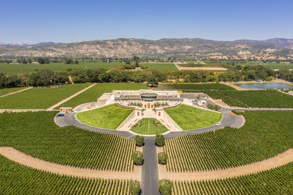 Aerial view of a large, symmetrically designed winery building surrounded by extensive, manicured vineyards in Napa Valley.