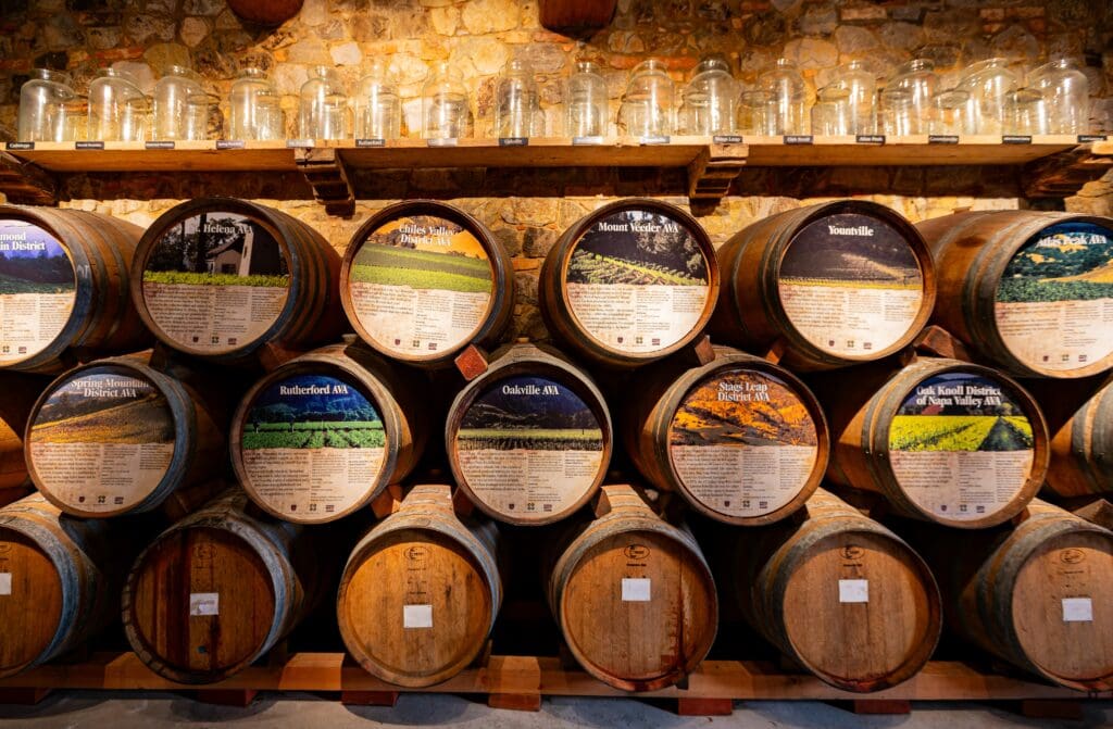Wall display of stacked wine barrels, each labeled with a distinct Napa Valley AVA and an image of a vineyard landscape.