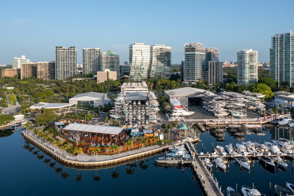 Aerial view of the Coconut Grove marina and waterfront restaurants in Miami, backed by dense high-rise apartment towers.