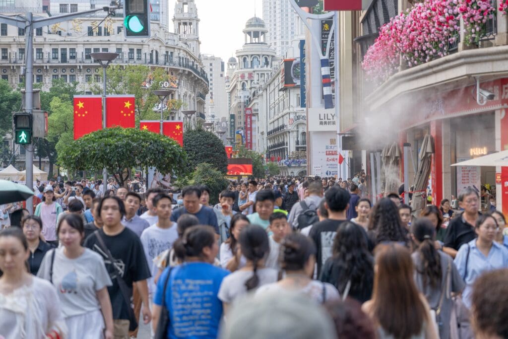 A massive crowd of pedestrians walking shoulder-to-shoulder on the historic Nanjing Road in Shanghai, decorated with Chinese flags.