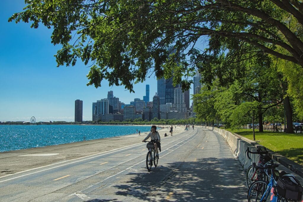 A cyclist rides on the Chicago Lakefront Trail with Lake Michigan and the city skyline.