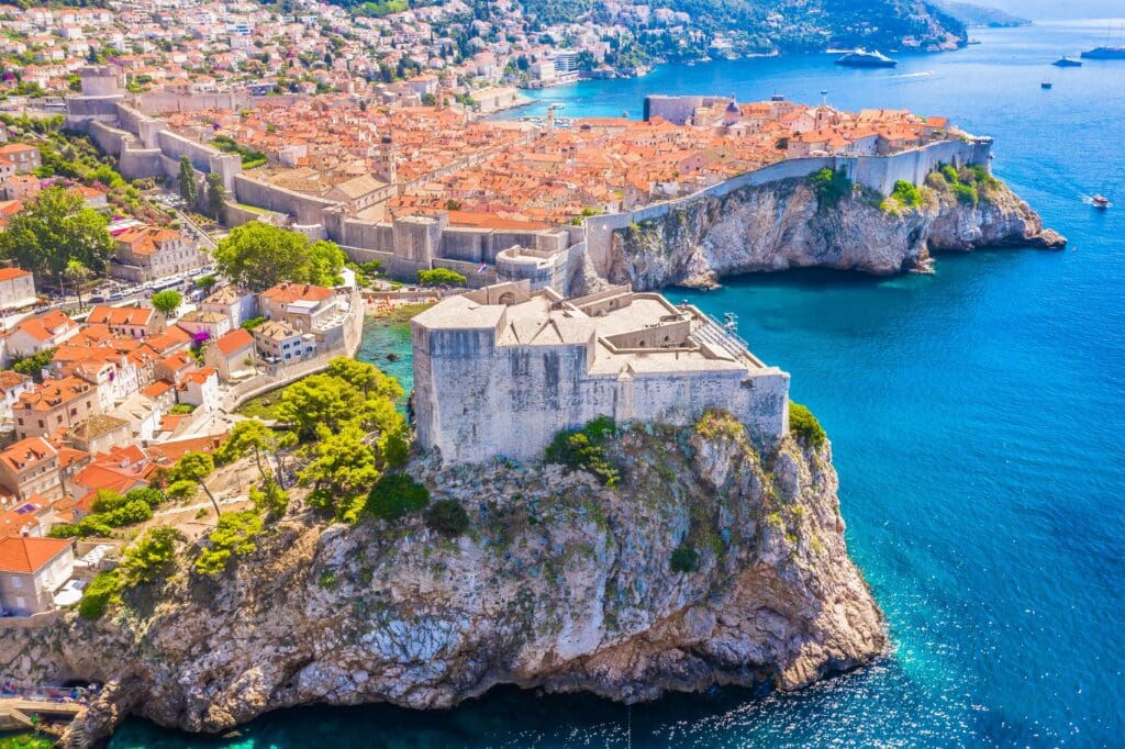 Aerial view of the massive stone Fort Lovrijenac situated on a sea cliff, overlooking the UNESCO-listed red-roofed Old Town of Dubrovnik, Croatia, and the Adriatic Sea.