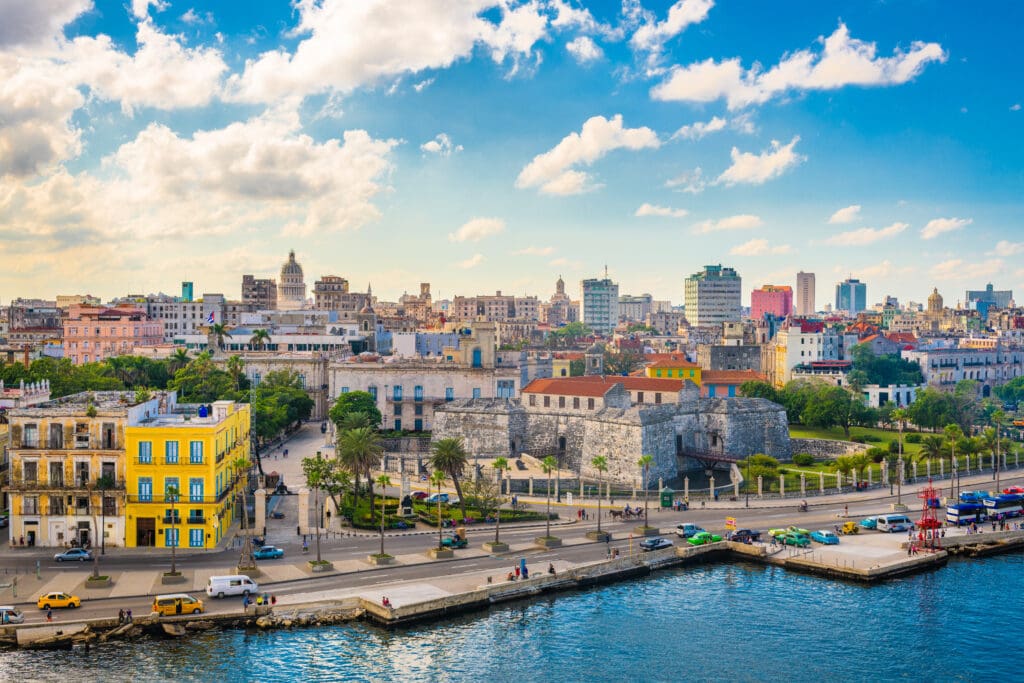 Wide, elevated view of the Havana, Cuba, downtown skyline and waterfront, featuring historic forts and colorful buildings along the Malecón.