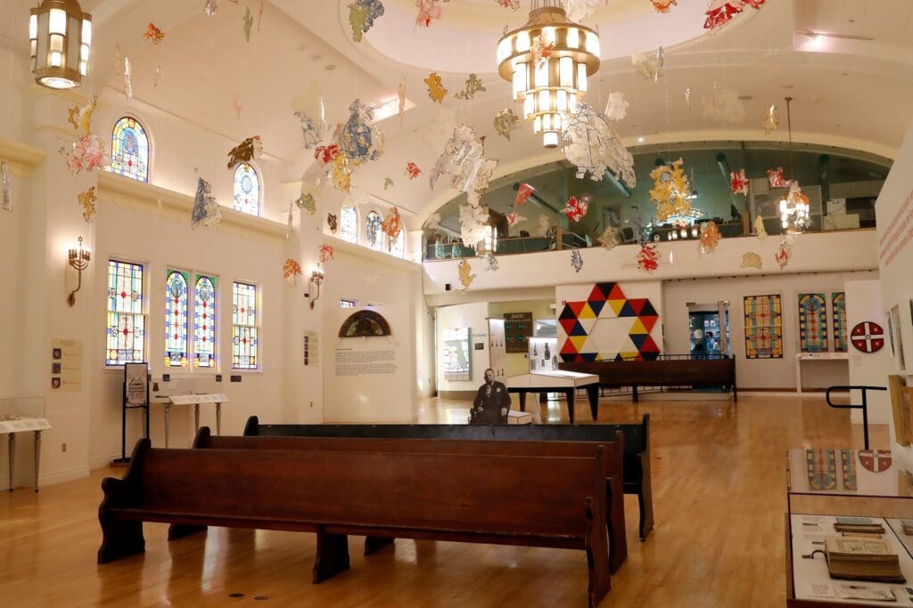 The main exhibition hall of the Jewish Museum of Florida, showing pews and stained-glass windows.