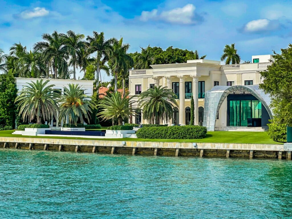 A white neoclassical luxury mansion on Miami's Star Island, featuring a modern glass annex and a waterfront pool.