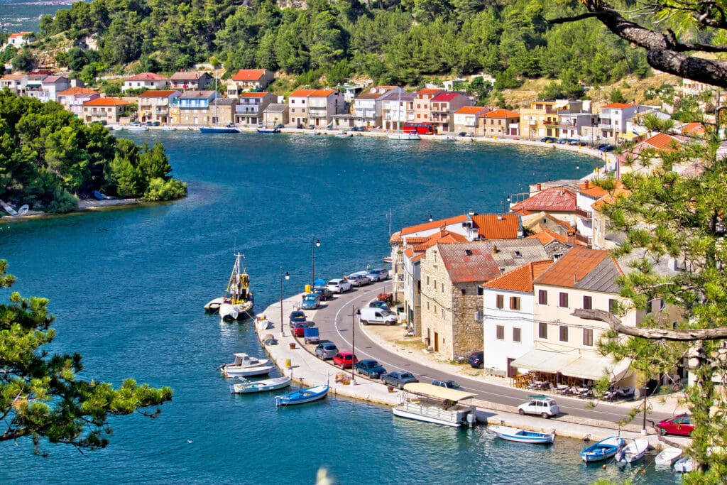 High-angle aerial view of the colorful waterfront of Novigrad, a Croatian fishing village situated in a deep, sheltered bay surrounded by green hills.