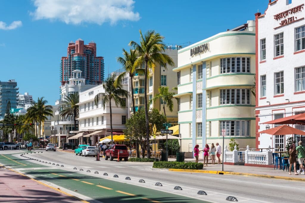 Ocean Drive in Miami's Art Deco District, showing historic hotels, palm trees, and people strolling along the sidewalk on a sunny day.