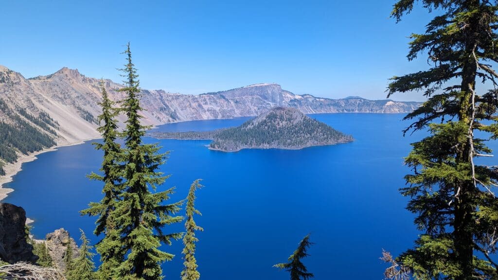 A scenic view of the deep blue Crater Lake and Wizard Island, framed by evergreen trees.