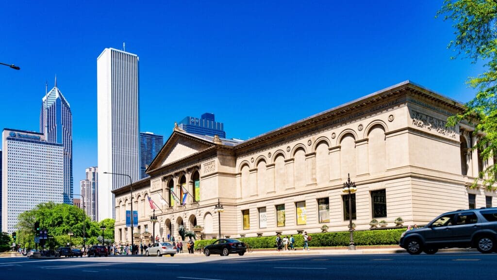 The classical facade of the Art Institute of Chicago on a sunny day with skyscrapers in the background.