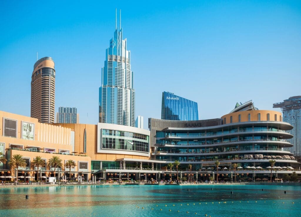 The Dubai Mall complex next to a large water feature, with modern skyscrapers in the background.
