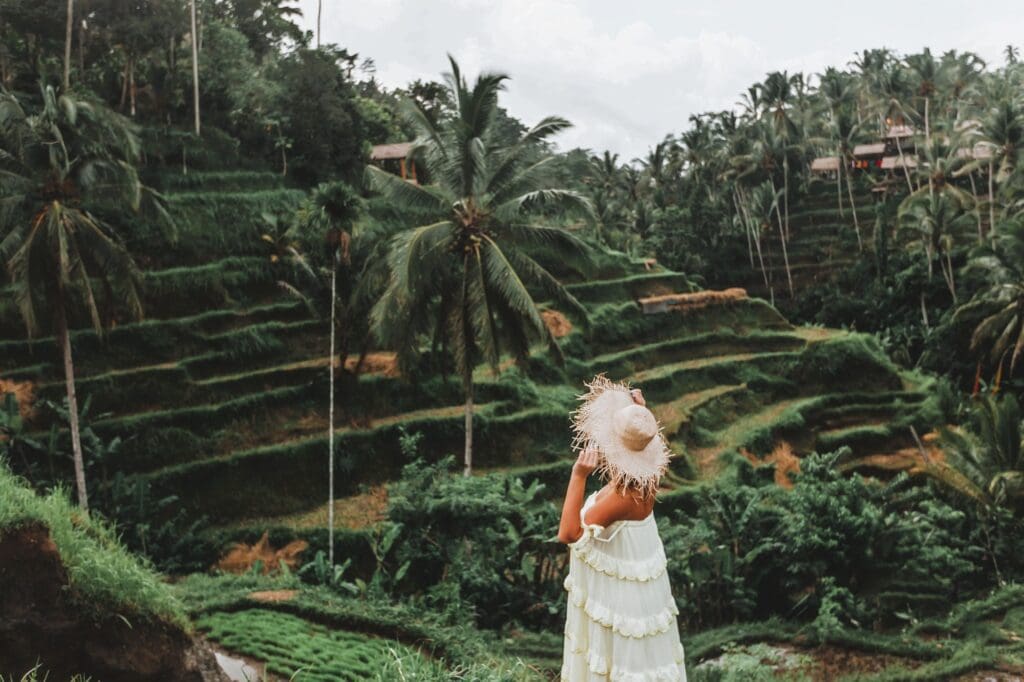 Woman in a straw hat overlooking the lush, green rice terraces of Ubud, Bali.