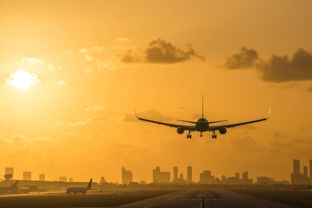 At sunrise, an airplane descends to land at Miami International Airport, with the Miami Downtown skyline as a stunning backdrop.